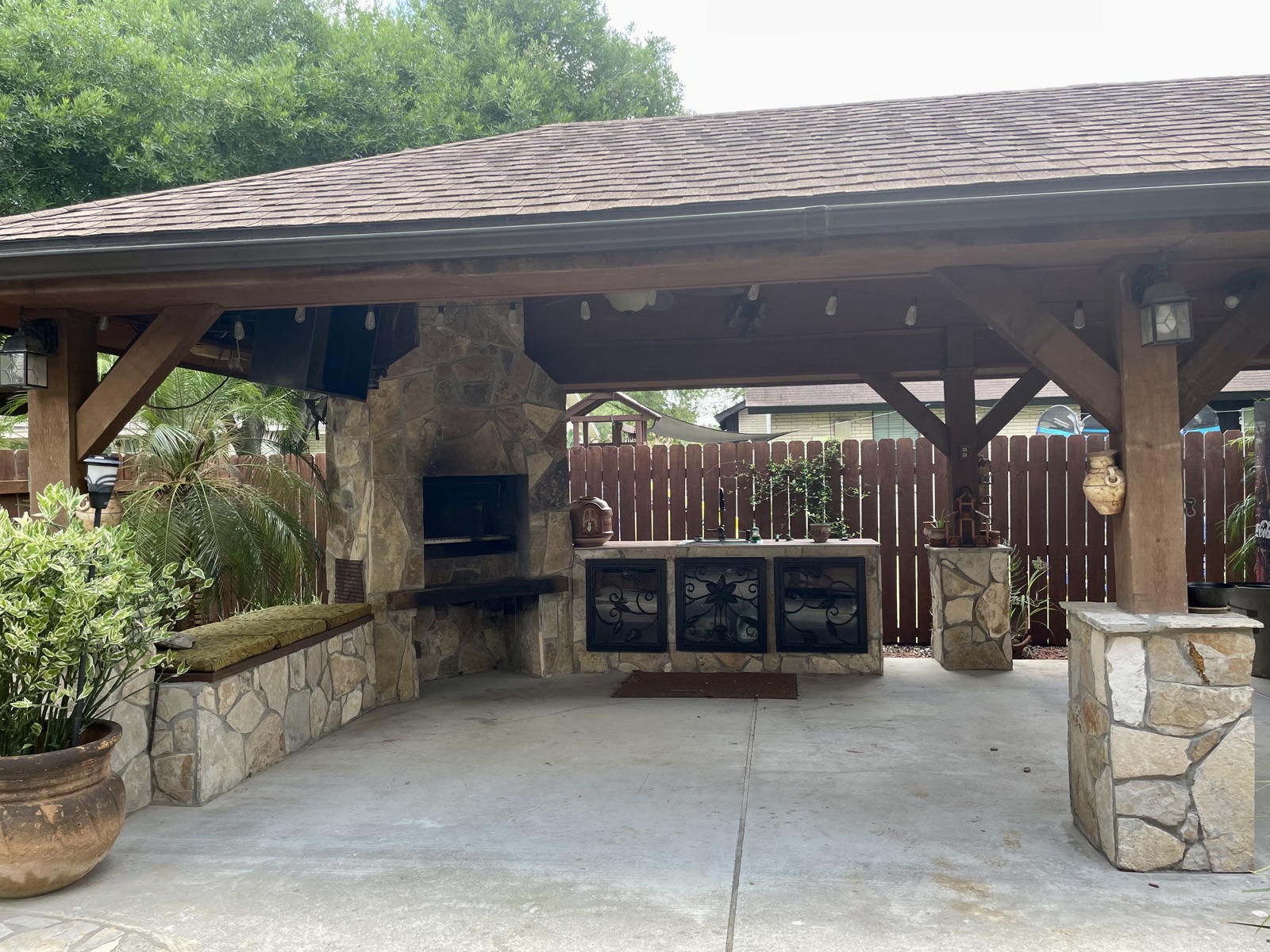 Covered outdoor kitchen pavilion with stone fireplace, built-in grill, and stamped concrete patio