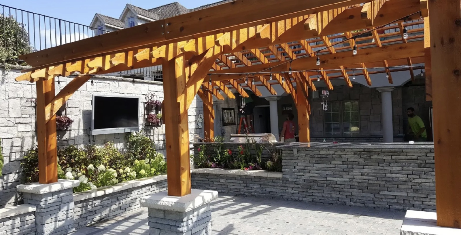 Cedar pergola over stone outdoor kitchen with paver patio