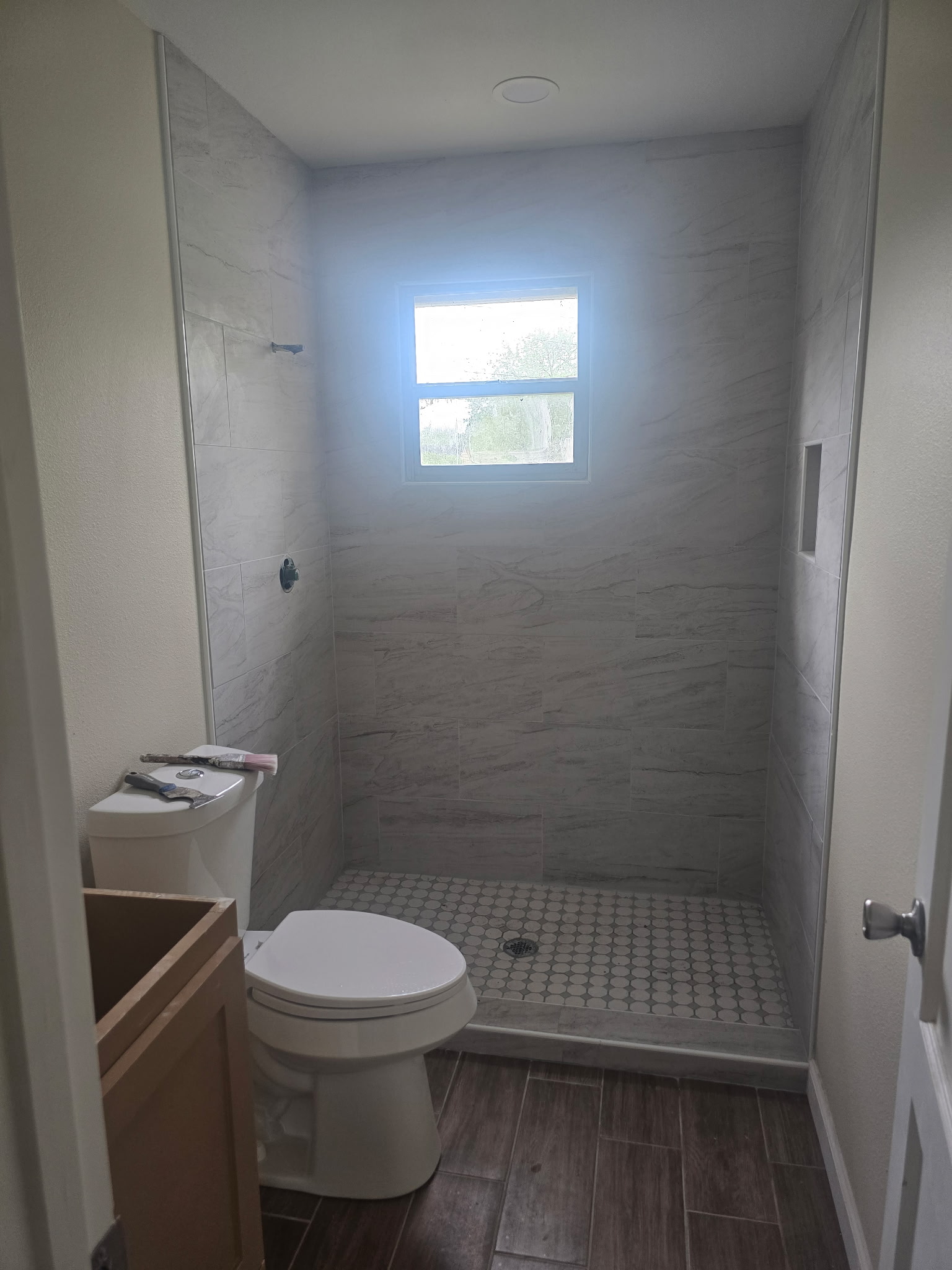 Renovated bathroom with marble-look tile shower and wood-grain tile floor